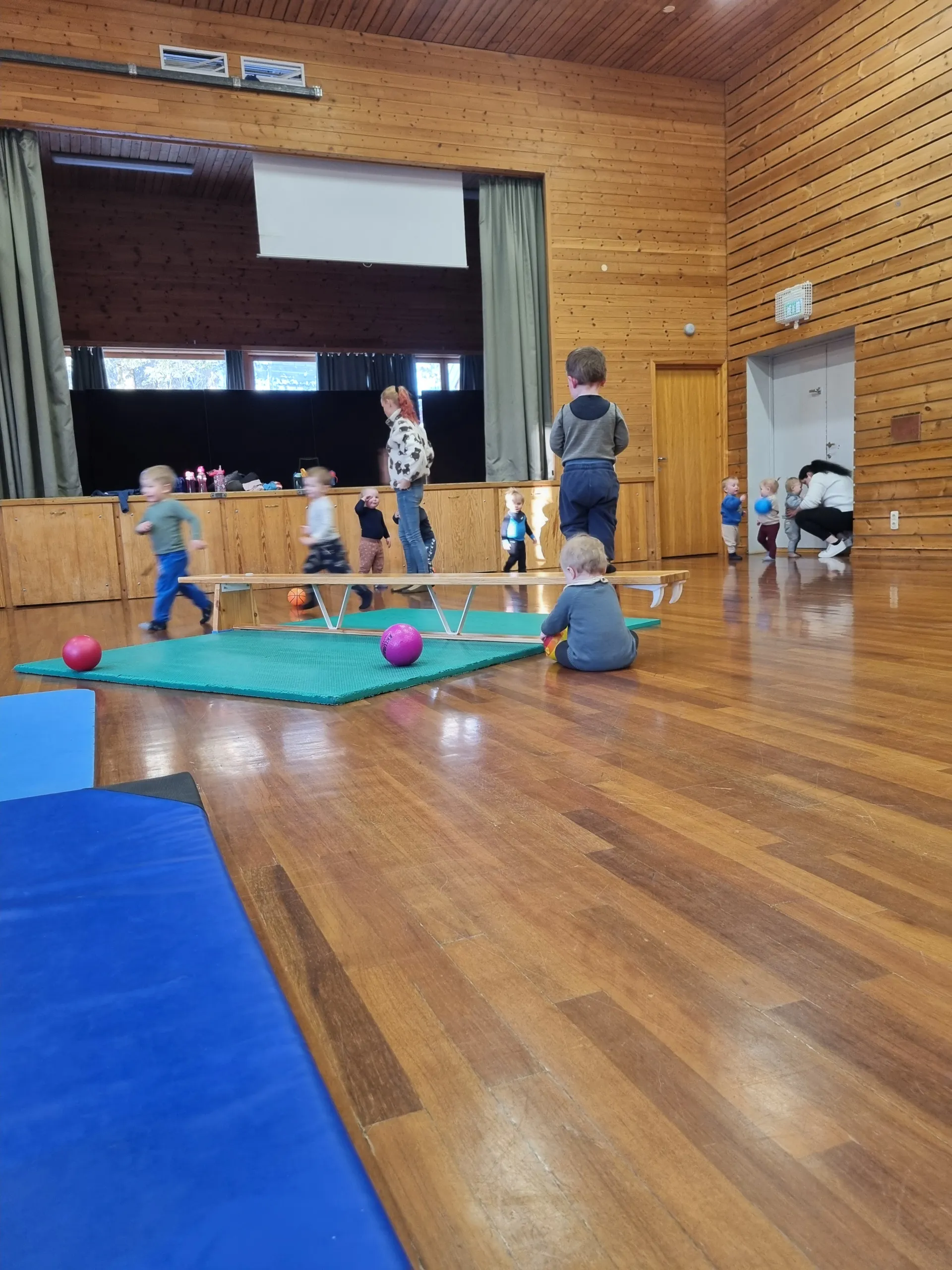 Barn leker med baller og balansebenk i gymsalen